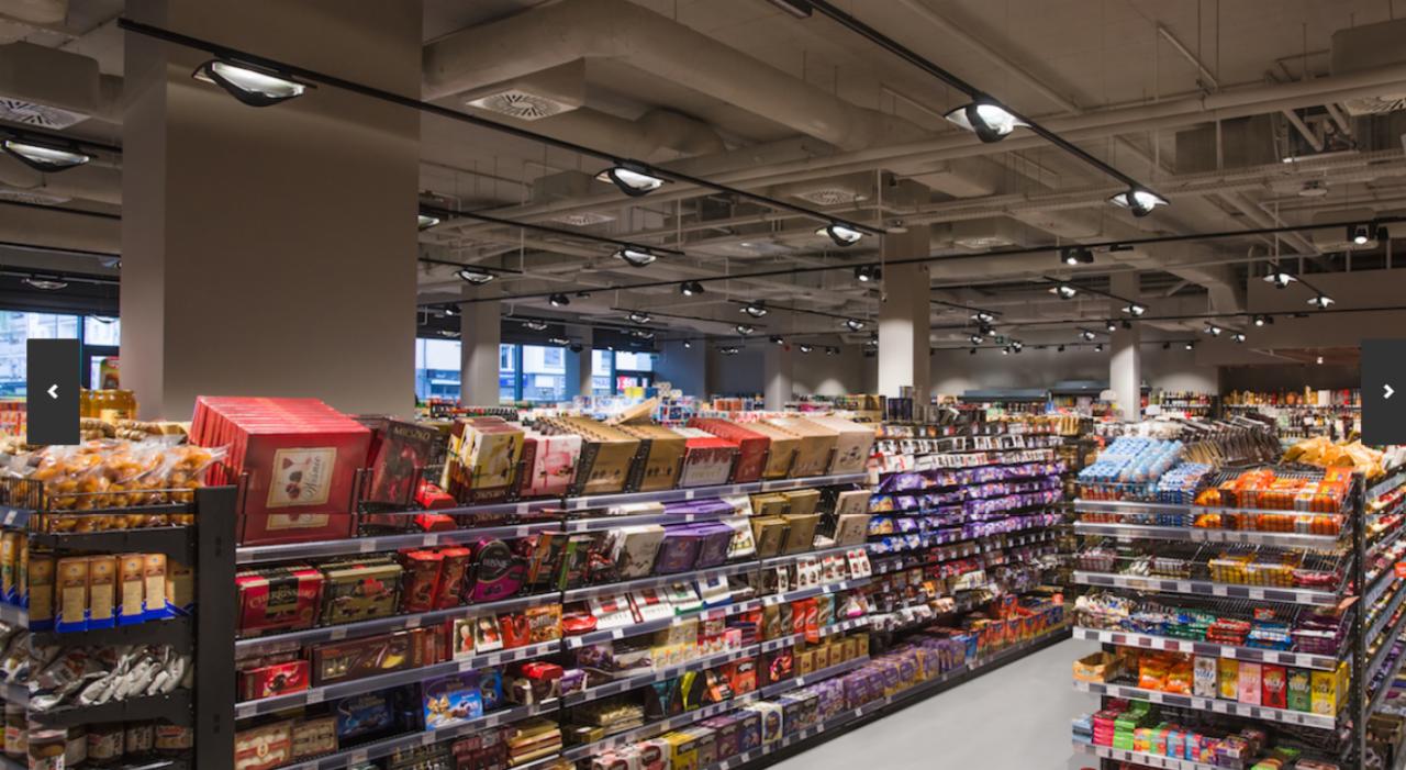 Równomierne rozmieszczenie punktowych lamp na szynoprzewodach w supermarkecie, oświetlających regały z towarami.