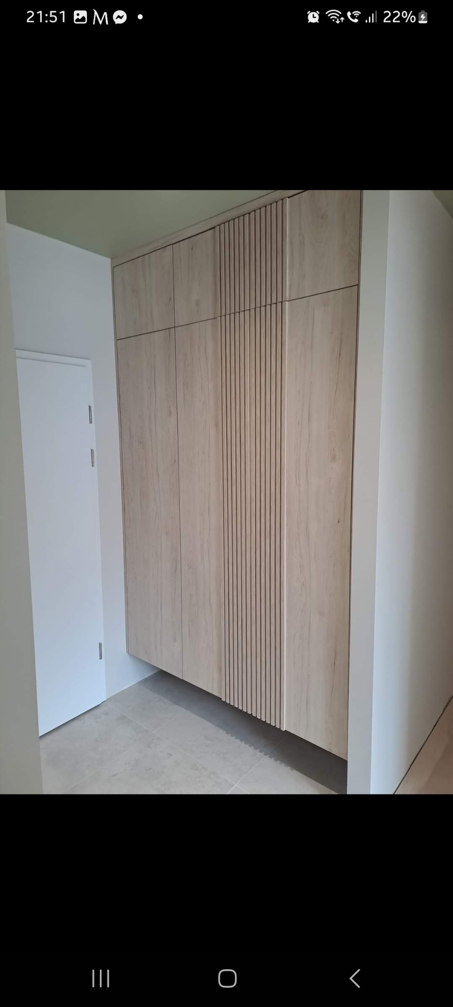 Szafa wnękowa z drewnopodobnymi frontami i pionowymi żłobieniami, zamontowana w korytarzu z szarą podłogą, widoczna biała ściana i drzwi.