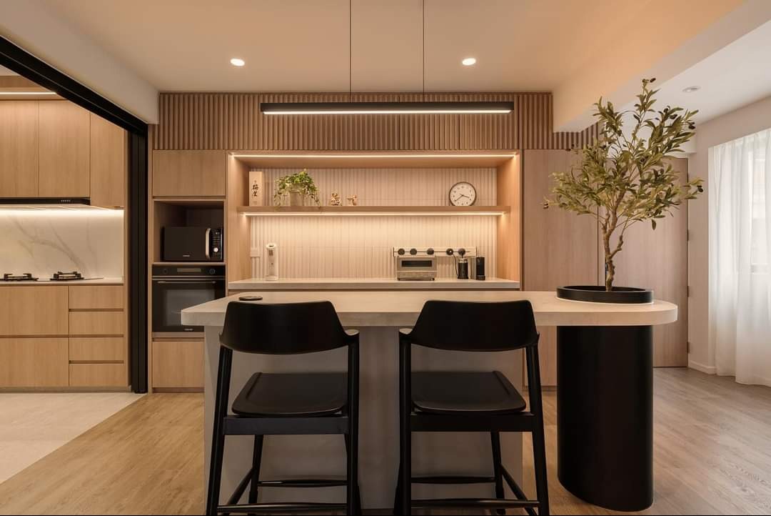 Jasna kuchnia z drewnianymi frontami, wyspą z czarnymi hokerami, oświetleniem LED i dekoracyjnym drzewkiem w doniczce.