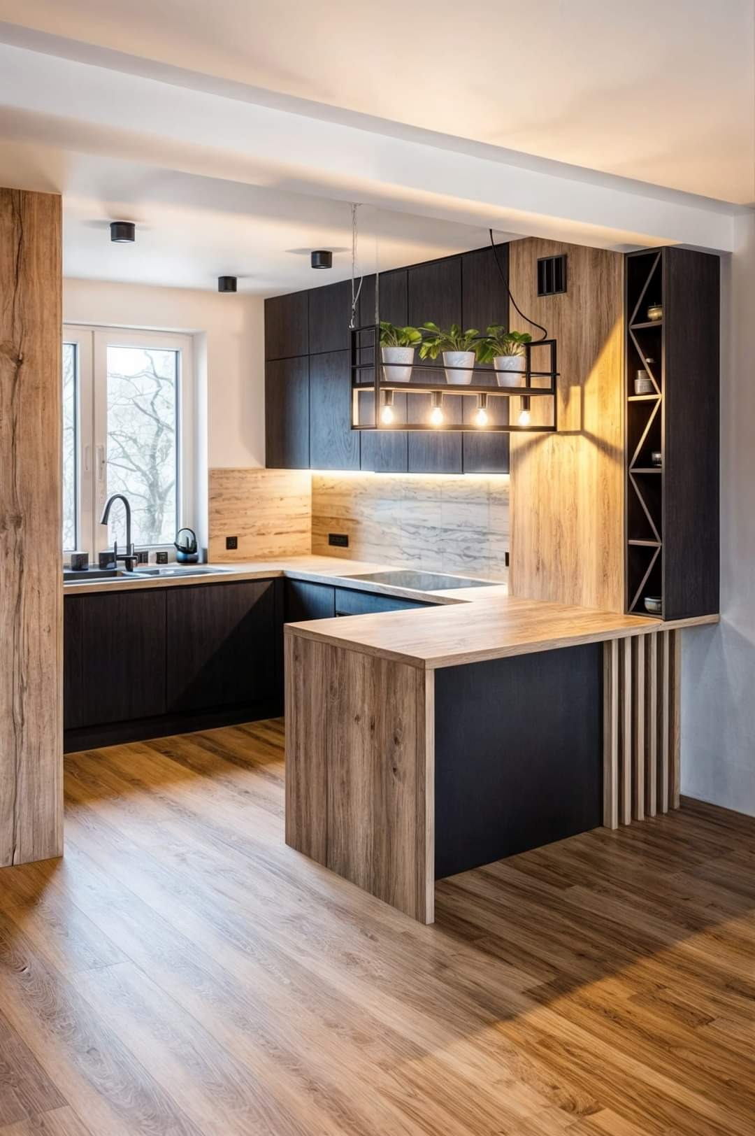 Nowoczesna kuchnia z ciemnymi szafkami i drewnianymi akcentami, wisząca lampa z roślinami, marmurowy backsplash, drewniana podłoga.