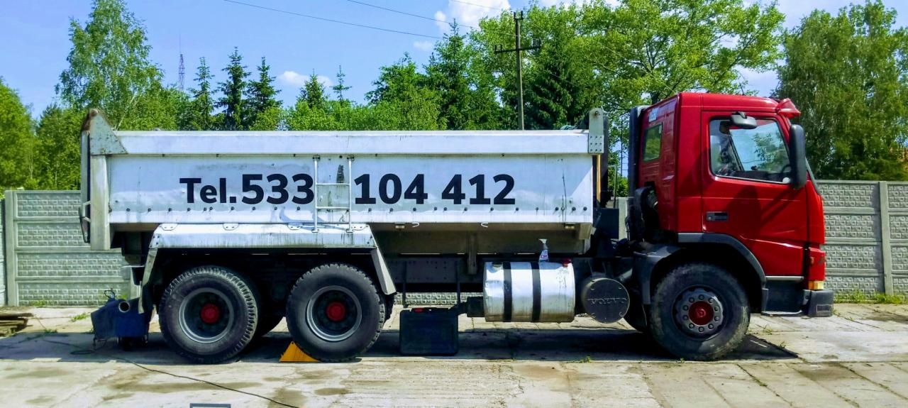 Czerwona ciężarówka z numerem telefonu na białej naczepie, zaparkowana na betonowym placu w słoneczny dzień.