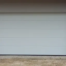 Nowoczesna, segmentowa brama garażowa w kolorze białym, z poziomymi panelami, zamontowana w jasnym budynku z kamienną podmurówką i ozdobnymi lampami po bokach.