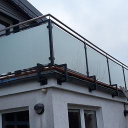 PORTAM Zwoliński - Barierka balkonowa z matowego szkła w czarnej metalowej ramie i z elementami ze stali nierdzewnej, widok z dołu, drabina oparta o ścianę budynku.