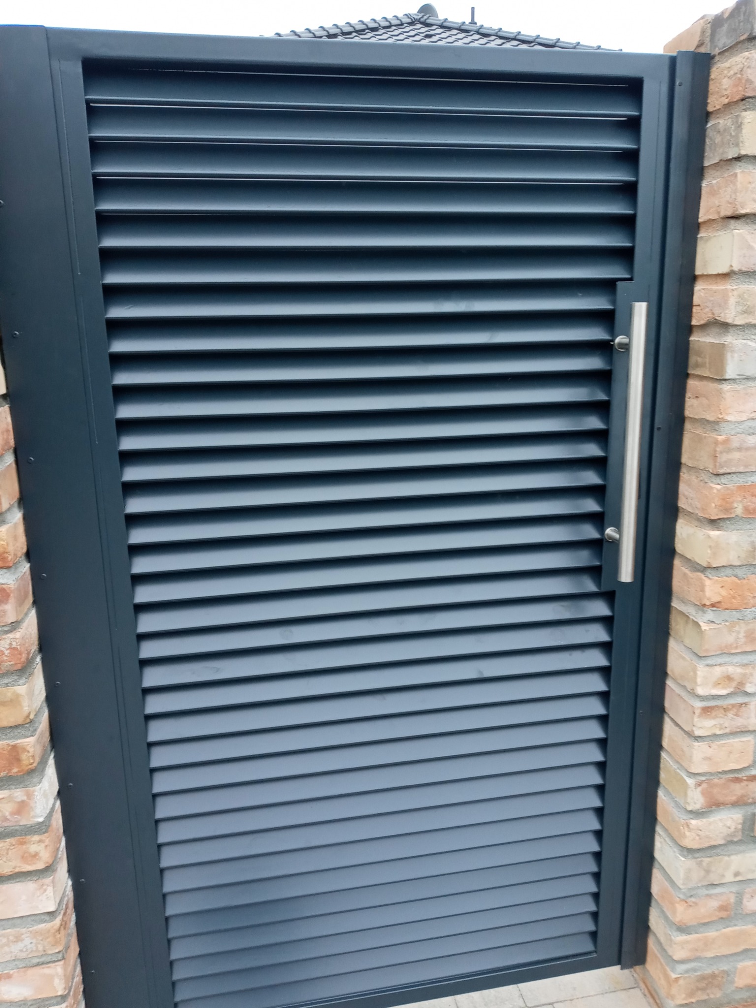 Nowoczesna, grafitowa brama z poziomymi lamelami, zamontowana na ceglanym słupku, z widocznym srebrnym uchwytem.