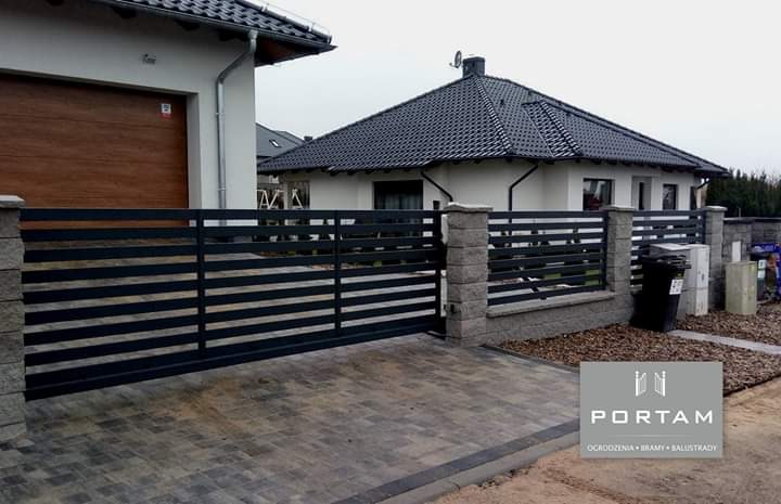 Nowoczesne, poziome przęsła metalowe tworzą ogrodzenie posesji z bramą przesuwną, uzupełnione kamiennymi słupkami i kostką brukową na podjeździe.