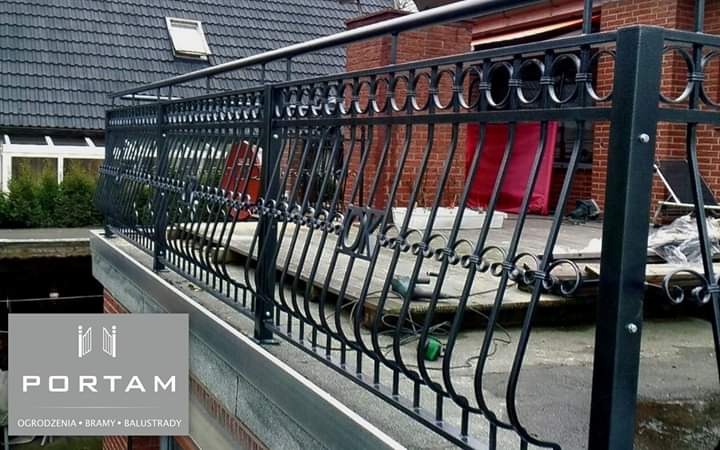 Czarna, metalowa balustrada balkonowa z dekoracyjnymi elementami w kształcie kółek, zamontowana na balkonie z ceglaną ścianą w tle.