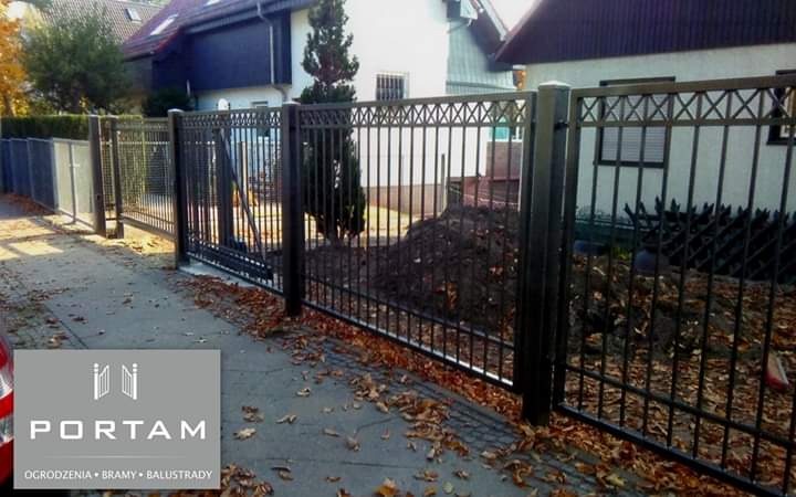 Czarne, metalowe ogrodzenie z dekoracyjnym wzorem krzyżyków w górnej części, widok z zewnątrz posesji, na chodniku leżą opadłe liście, w lewym dolnym rogu widoczne logo firmy Portam.