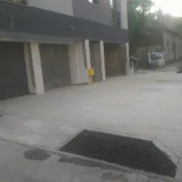 Nowa, jasnoszara nawierzchnia z betonowych płyt przed budynkiem z garażami; widoczny fragment rabaty z czarną ziemią i elementy budynku w tle.