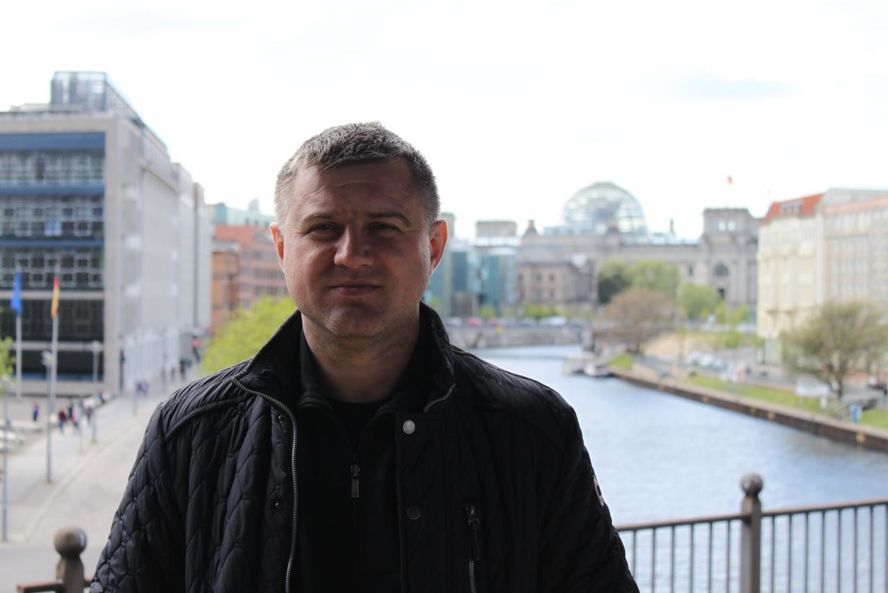 Portret mężczyzny w czarnej kurtce na tle panoramy Berlina z Reichstagiem i rzeką Sprewą