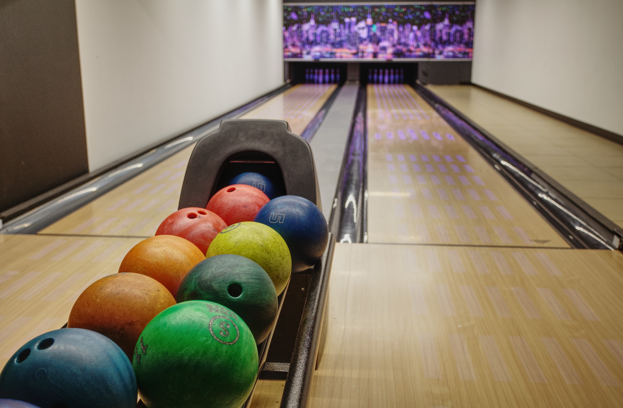 Rząd kolorowych kul do kręgli w podajniku, w tle tor do gry z podświetlanym ekranem.