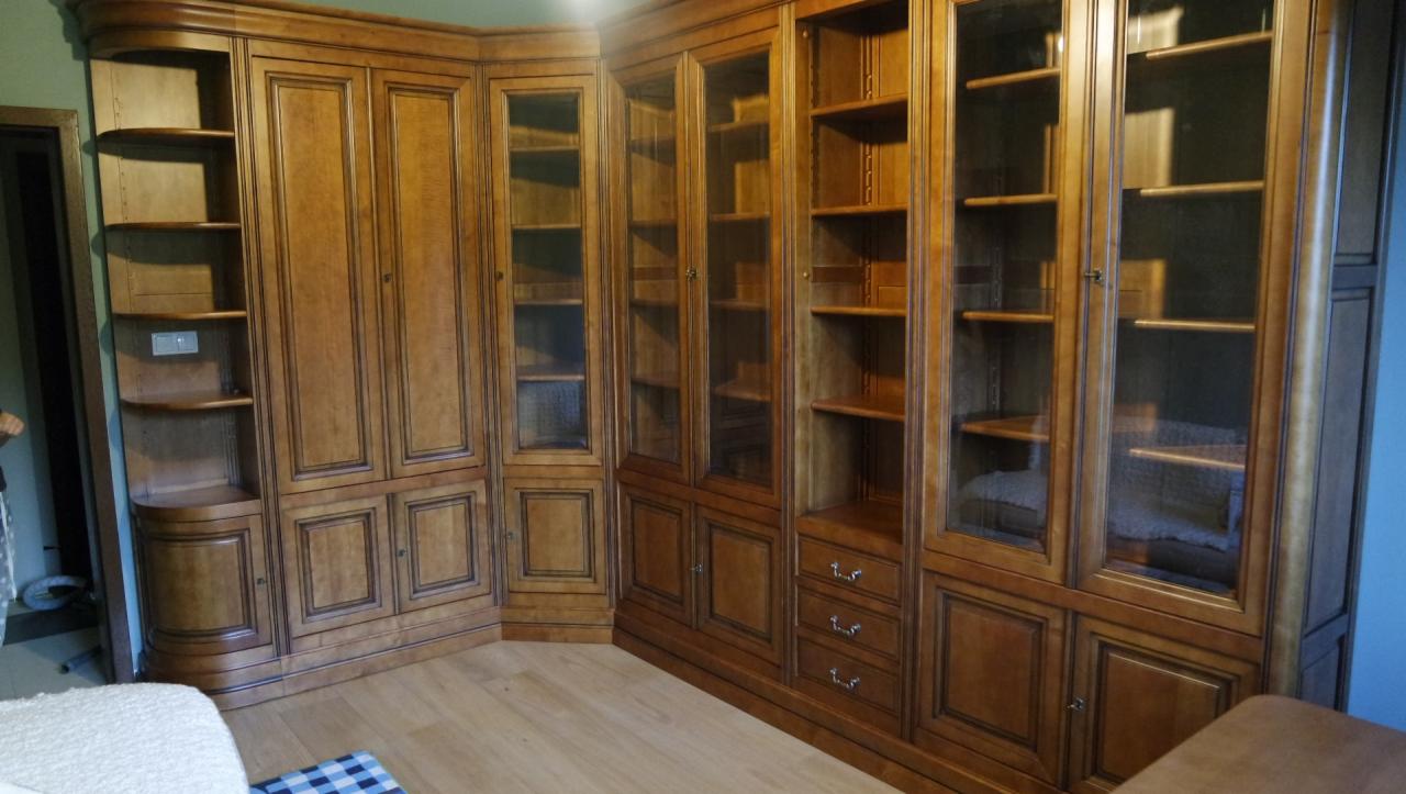 Duża, narożna biblioteka z drewna w odcieniach brązu, z przeszklonymi witrynami i otwartymi półkami, dopasowana do kąta pokoju, z widocznymi trzema małymi szufladami w dolnej części.
