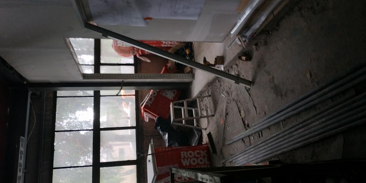 Wnętrze w trakcie remontu z widoczną ścianą z płyty karton gips, oknem z czarnymi szprosami, metalowymi profilami i materiałami izolacyjnymi Rockwool.
