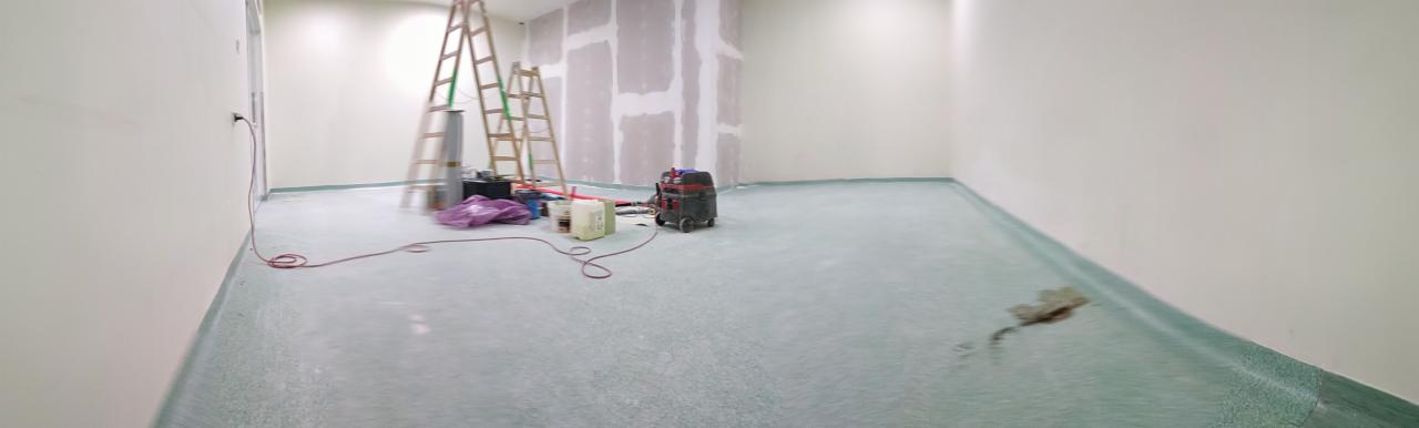 Wnętrze w trakcie prac przygotowawczych: częściowo wykończone ściany z płyt kartonowo-gipsowych, zabezpieczona folią podłoga, drabiny, odkurzacz przemysłowy i narzędzia.