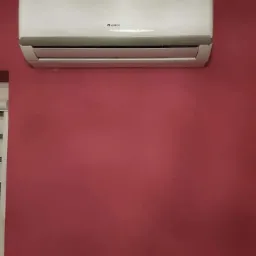 Biała jednostka klimatyzacji Gree zamontowana na bordowej ścianie w pomieszczeniu.