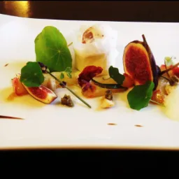 Elegancko podane danie z figami, pianką, ziołami i sosem balsamicznym na białym, prostokątnym talerzu.