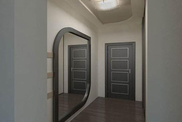 Korytarz z szarymi drzwiami z prostokątnymi panelami obwiedzionymi srebrną listwą i asymetrycznym lustrem w ciemnej ramie.