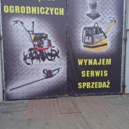 Baner reklamowy na garażu z ofertą wynajmu, serwisu i sprzedaży narzędzi ogrodniczych, w tym glebogryzarki, nożyc do żywopłotu, ubijaka i zagęszczarki.
