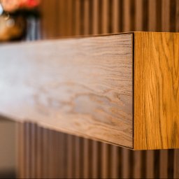 DREAMS DESIGN STUDIO - Drewniana, wisząca szafka z szufladą w ciepłym odcieniu dębu, zamontowana na ścianie z pionowych paneli. Minimalistyczny design, detale wykończenia.