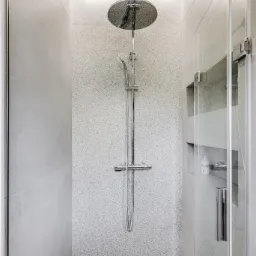 Nowoczesna kabina prysznicowa z deszczownicą, szklanymi drzwiami i półkami w ścianie. Minimalistyczny design w odcieniach szarości i bieli, z subtelnym oświetleniem LED.