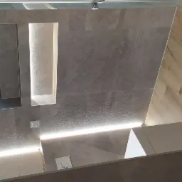 Nowoczesna łazienka z drewnopodobną podłogą, szarymi płytkami ściennymi, oknem dachowym i podświetlaną wnęką w ścianie.