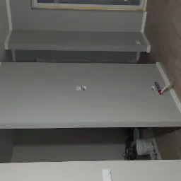 Świeżo pomalowane na szaro wnętrze z widocznymi listwami przypodłogowymi, gniazdkami elektrycznymi i fragmentem podłogi z paneli, z widocznymi narzędziami i pojemnikami pod ścianą.