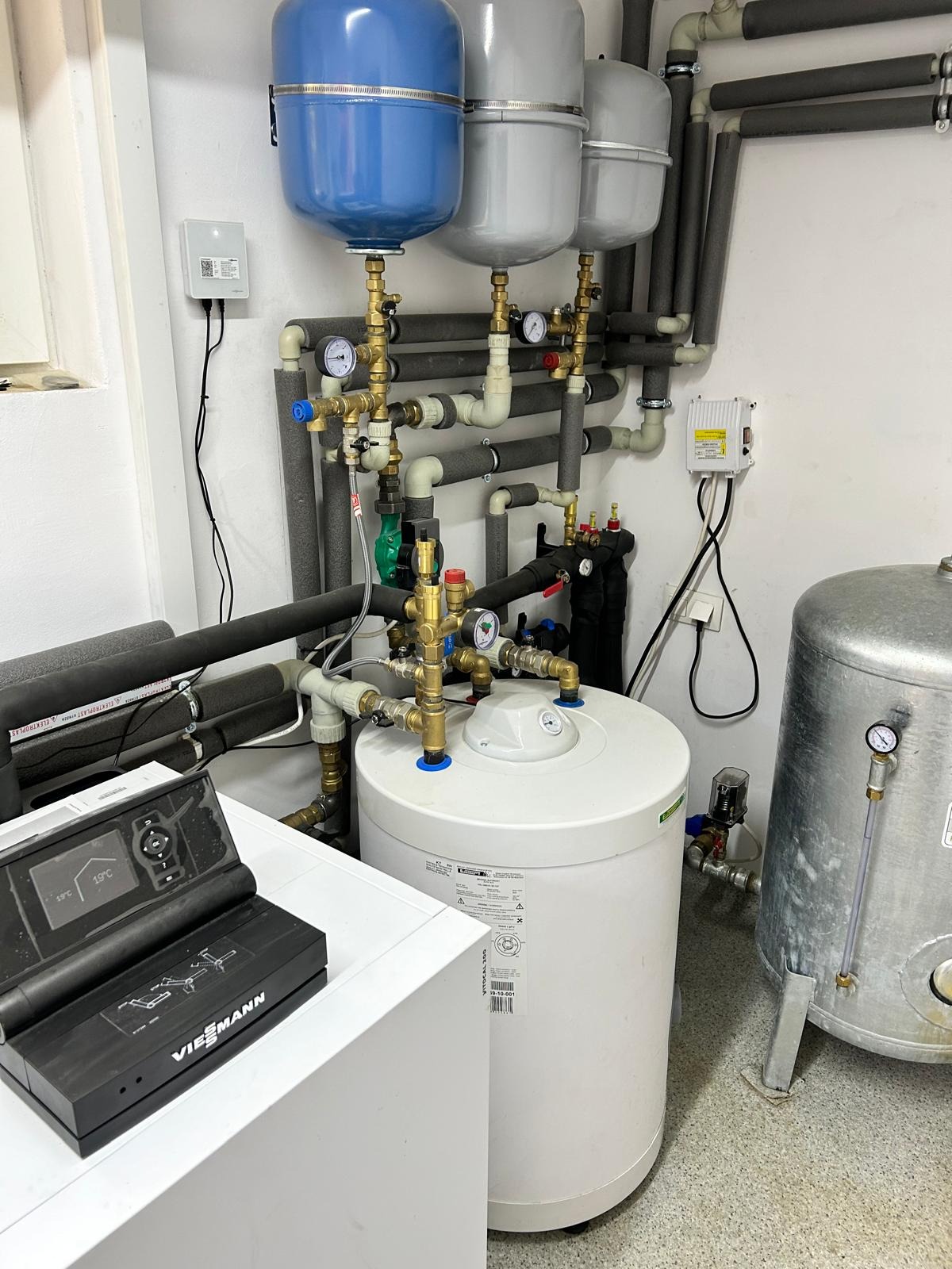 Kotłownia z bojlerem, zbiornikami wyrównawczymi i rurami w izolacji. Widoczny panel sterowania Viessmann. Manometry i zawory. Ujęcie w pomieszczeniu.