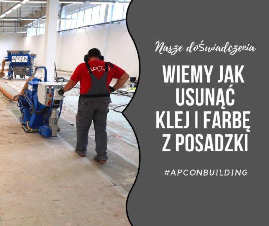 Pracownik w czerwonej koszulce i szarych spodniach roboczych obsługuje niebieską maszynę do usuwania kleju i farby z betonowej posadzki w hali przemysłowej. Widoczny efekt częściowego oczyszczenia...