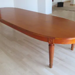 Rozkładany stół jadalny z drewna o owalnym blacie i toczonych nogach, widoczne łączenia blatu, na jasnej drewnianej podłodze.