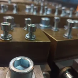 Detaliczne ujęcie metalowych śrub z podkładkami na obrobionej powierzchni, widoczna precyzja wykonania i sześciokątne gniazdo śruby.