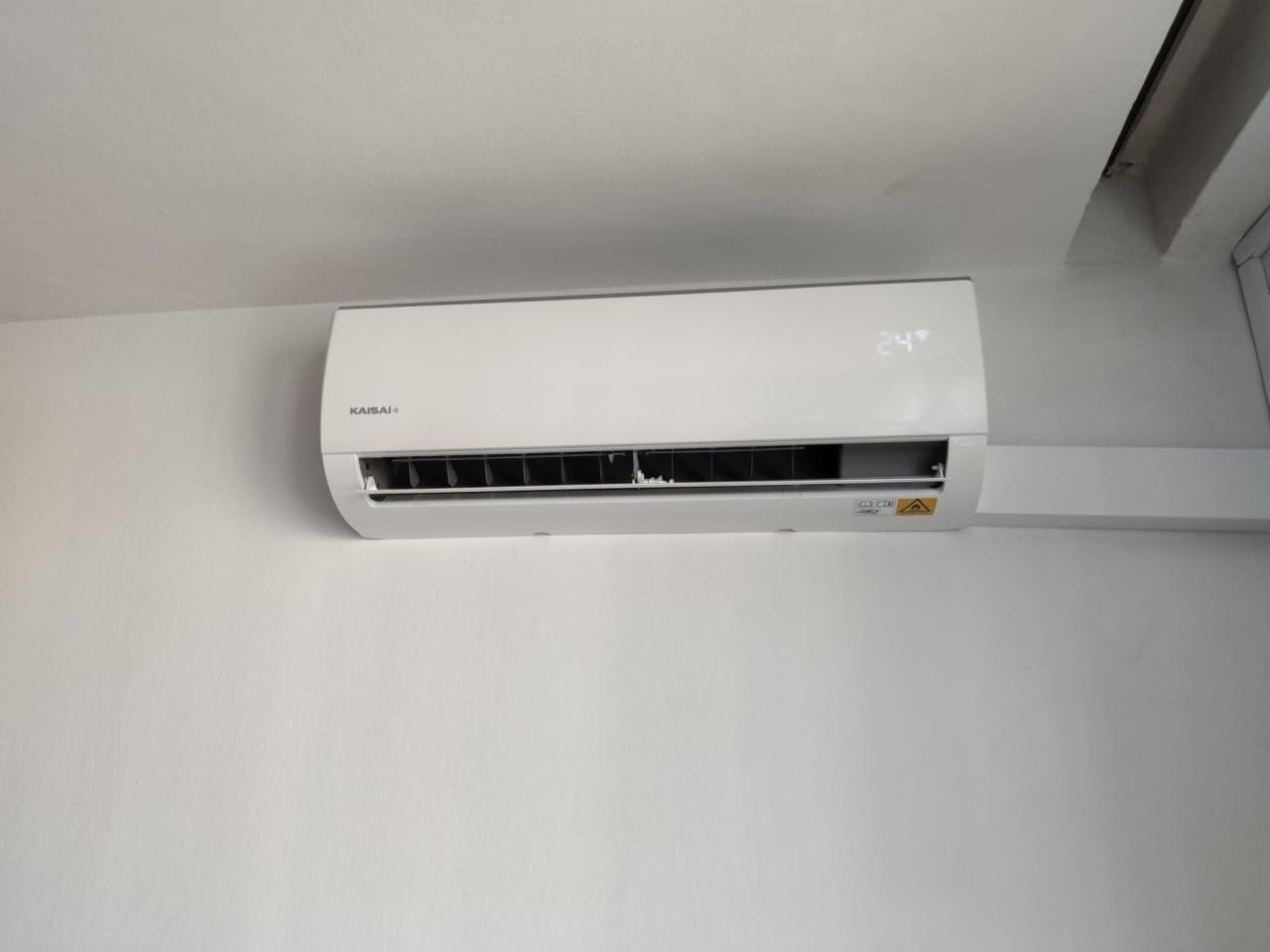 Biała klimatyzacja Kaisai zamontowana na białej ścianie, wyświetlająca temperaturę 24 stopnie Celsjusza, z widocznym fragmentem sufitu i listwy przypodłogowej.