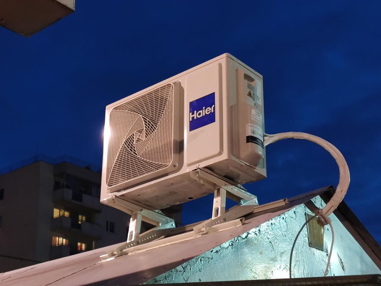 Zewnętrzna jednostka klimatyzacji Haier zamontowana na dachu budynku, widoczna wieczorem na tle ciemnego nieba.