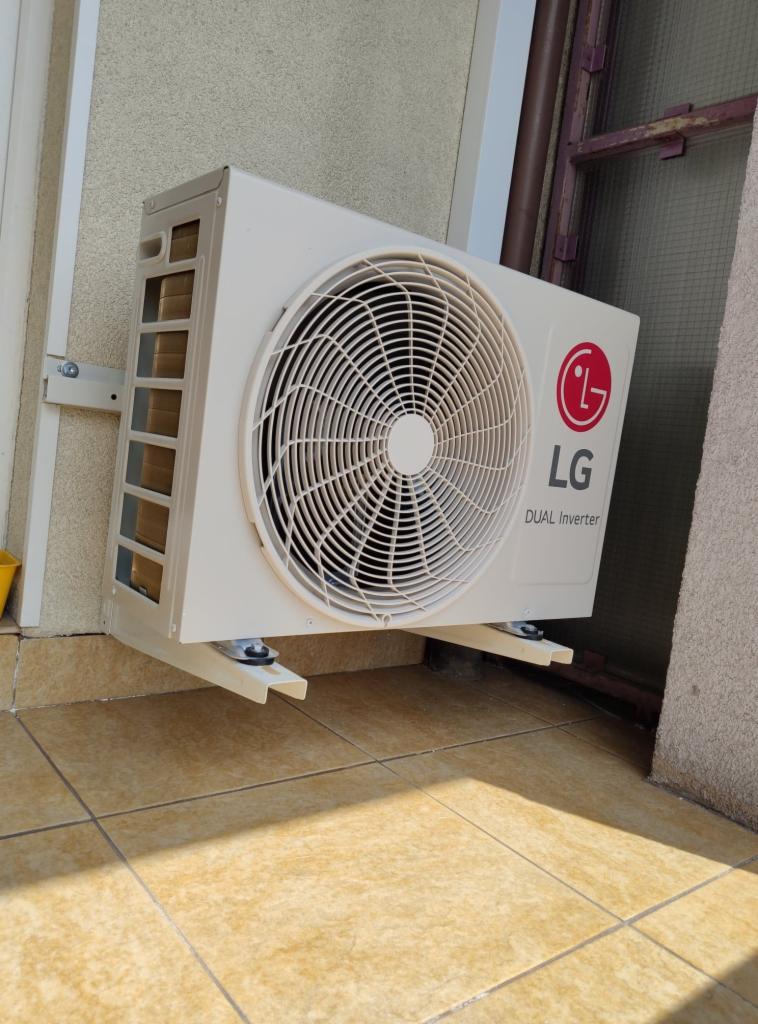 Biała jednostka zewnętrzna klimatyzacji LG Dual Inverter zamontowana na jasnobeżowej elewacji, widoczne mocowania i fragment brązowej rury.