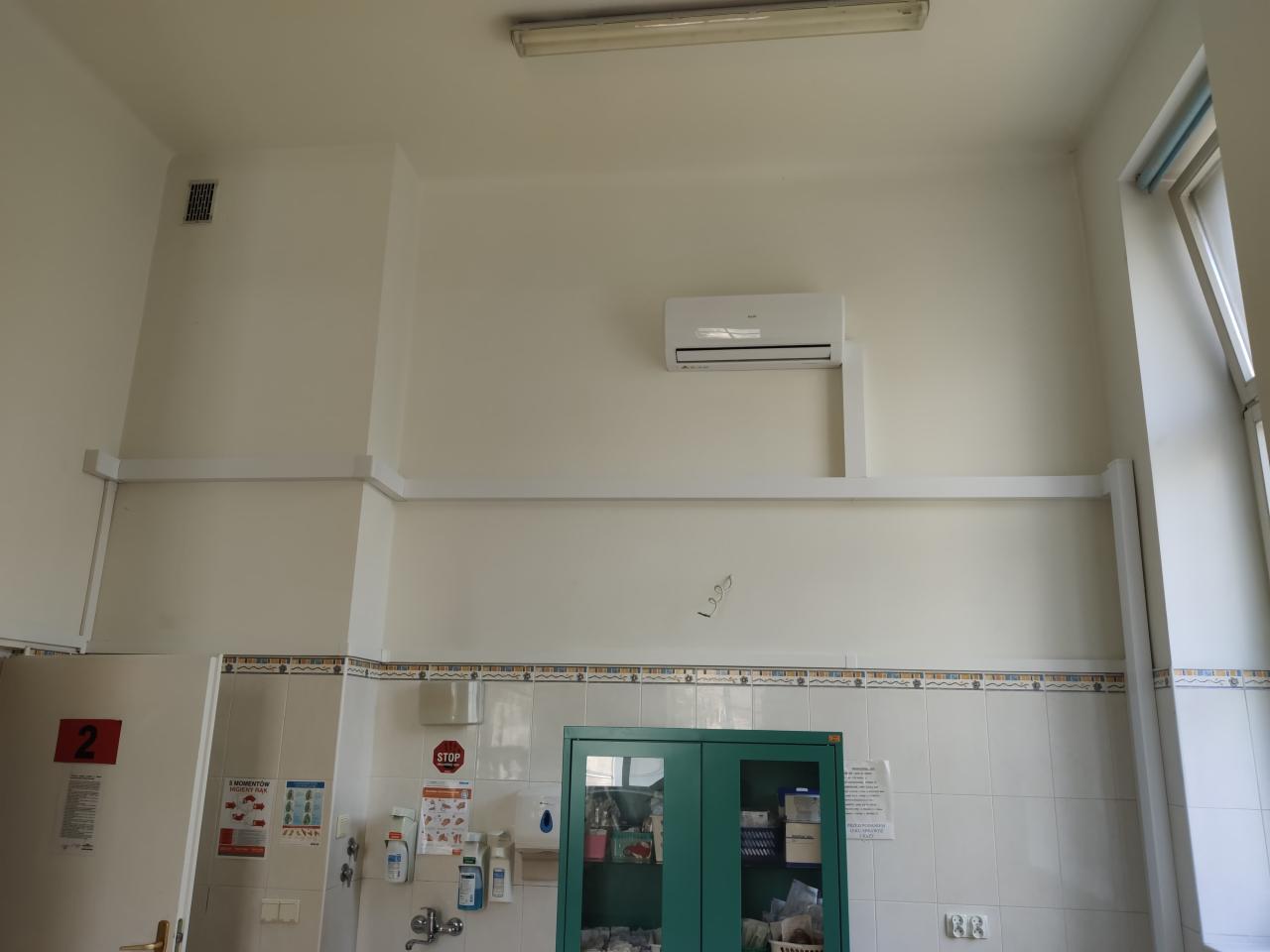 Biała klimatyzacja split zamontowana na ścianie w pomieszczeniu z kafelkami i szafkami, widok z dołu.