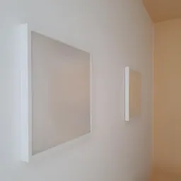 Dwa panele LED z białymi ramkami zamontowane na białej ścianie, z widocznym fragmentem ściany pomalowanej na pomarańczowo i oknem w tle.