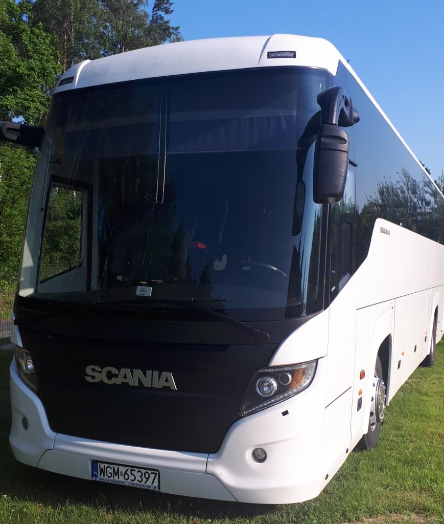 Biały autokar marki Scania z widoczną tablicą rejestracyjną WGM-65397, stojący na trawie w słoneczny dzień.