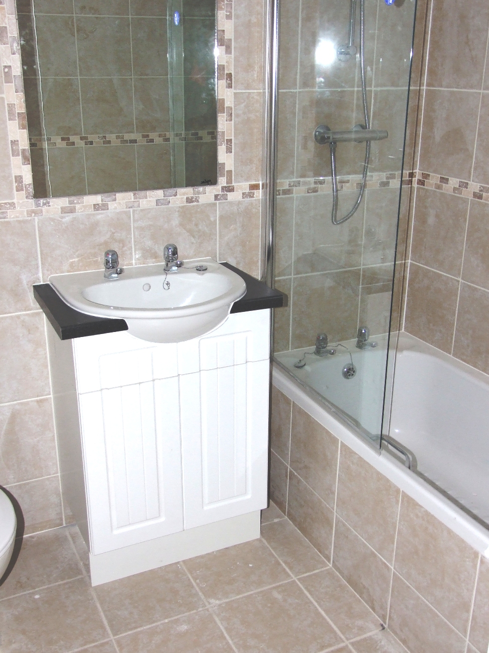 Wykończona łazienka z beżowymi płytkami, umywalką z szafką, lustrem z mozaikową ramą i kabiną prysznicową z wanną.