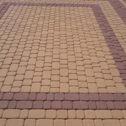 Ułożona kostka brukowa w dwóch odcieniach brązu tworząca geometryczny wzór na powierzchni chodnika.