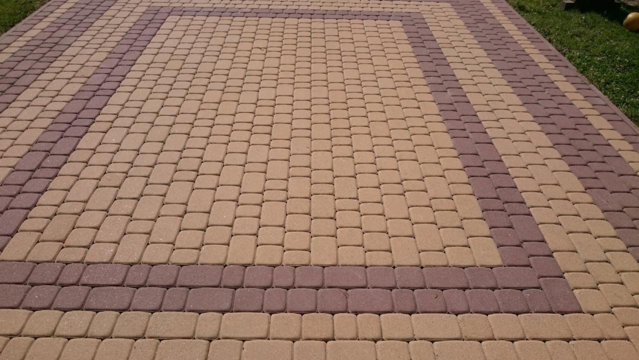 Ułożona kostka brukowa w dwóch odcieniach brązu tworząca geometryczny wzór na powierzchni chodnika.