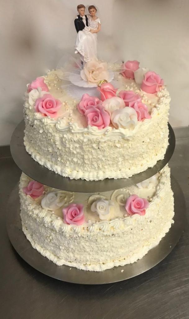 Dwupiętrowy tort weselny z figurką pary młodej, zdobiony kremem, białymi wiórkami, różowymi i białymi różami oraz perłami, wykonany w Mikołowie.