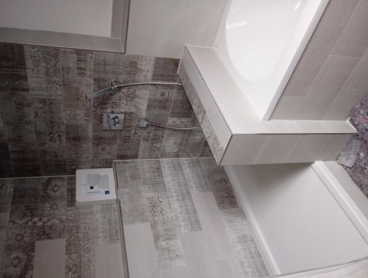 Wykończona łazienka z mozaikowymi płytkami na ścianie, białą wanną z obudową z jasnych płytek i chromowaną baterią prysznicową.