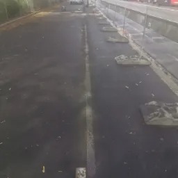 Świeżo wylany asfalt na ulicy miejskiej, widoczne bariery ochronne i sprzęt budowlany w tle.