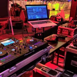 Sprzęt DJ-ski Pioneer, laptop z oprogramowaniem, mikser dźwięku i oświetlenie sceniczne w sali bankietowej podczas wydarzenia.