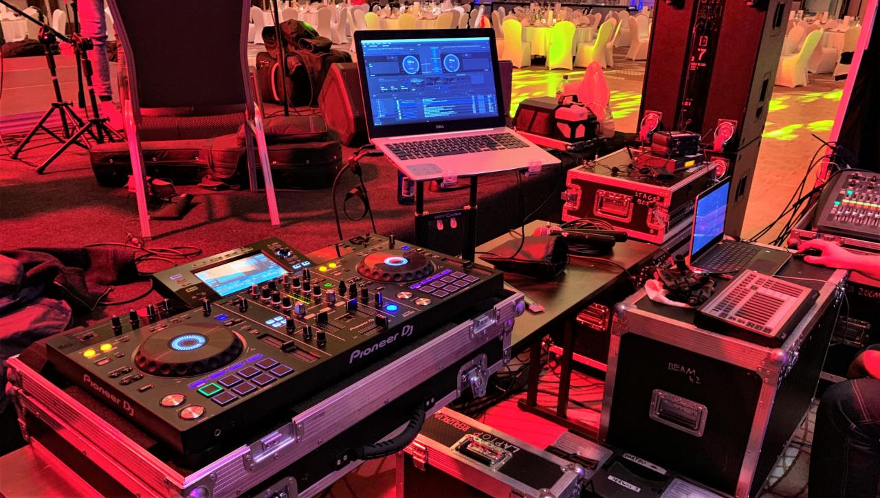 Sprzęt DJ-ski Pioneer, laptop z oprogramowaniem, mikser dźwięku i oświetlenie sceniczne w sali bankietowej podczas wydarzenia.