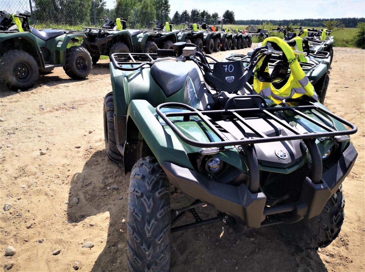 Rząd zielonych quadów Yamaha na piaszczystym terenie, z numerem 70 na przednim panelu jednego z nich i odblaskową kamizelką na kierownicy.