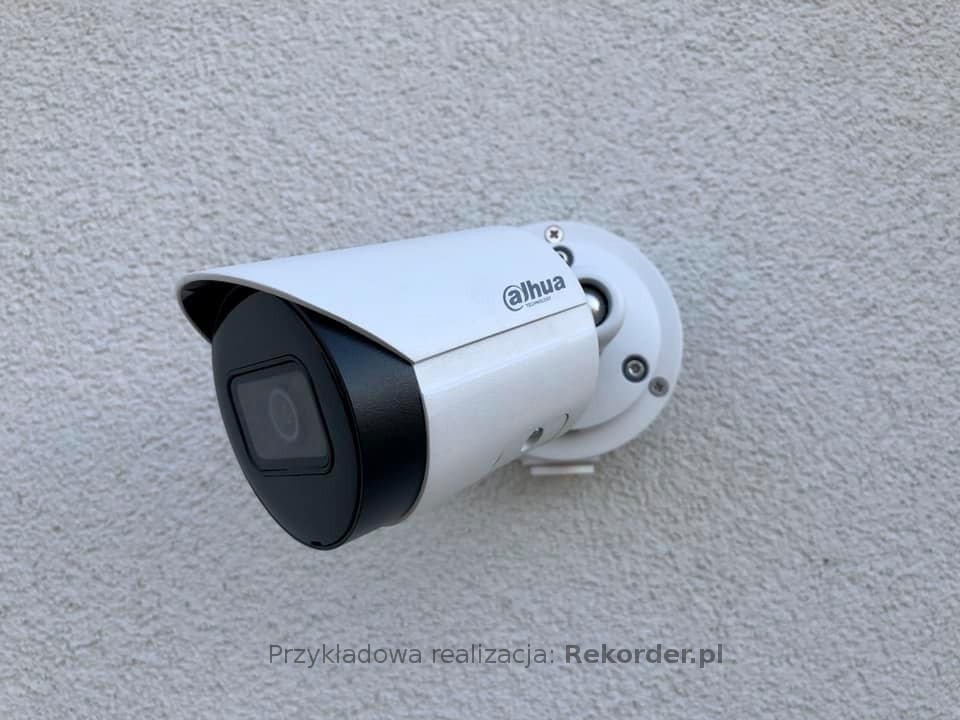 Biała kamera monitoringu Dahua zamontowana na szorstkiej, jasnej ścianie zewnętrznej budynku.