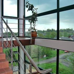 Omega Top Sp. z o.o. - Wnętrze z dużymi oknami PCV z widokiem na zewnątrz, schody z terakoty z metalową balustradą, doniczka z rośliną na podwyższeniu.
