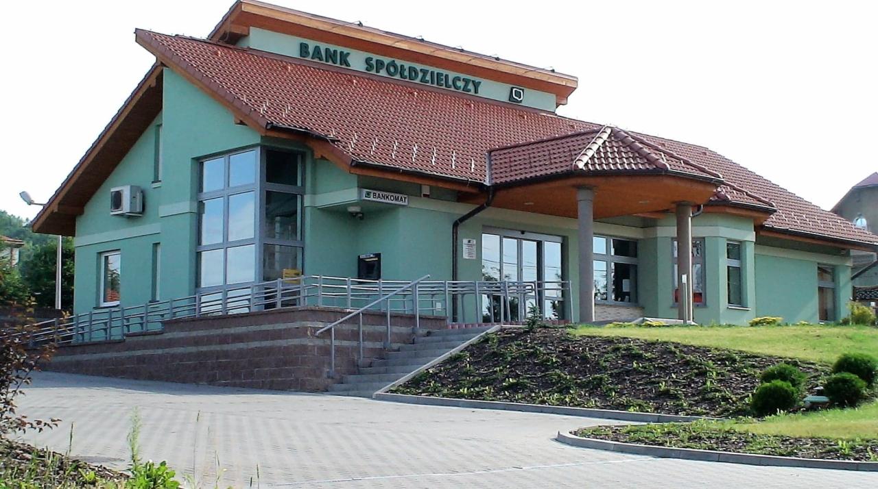 Budynek Banku Spółdzielczego z dużymi oknami na fasadzie, schodami z barierkami i bankomatem przy wejściu.