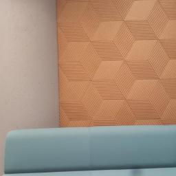 TRADING sp. z o.o. - Teksturowana ściana z geometrycznym wzorem 3D w odcieniach brązu, zestawiona z błękitną sofą i beżowym pufem, tworząc nowoczesne wnętrze.