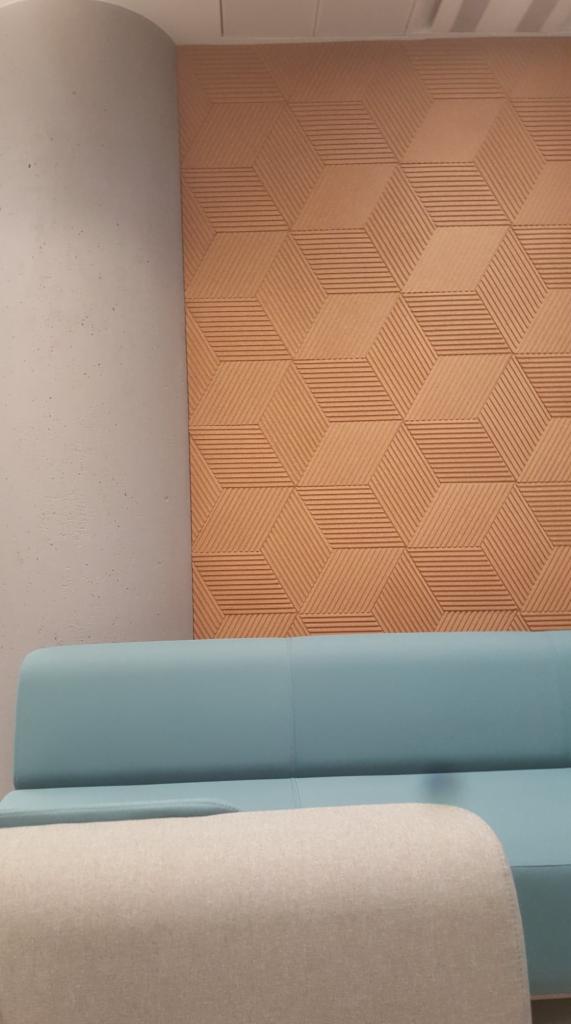 Teksturowana ściana z geometrycznym wzorem 3D w odcieniach brązu, zestawiona z błękitną sofą i beżowym pufem, tworząc nowoczesne wnętrze.