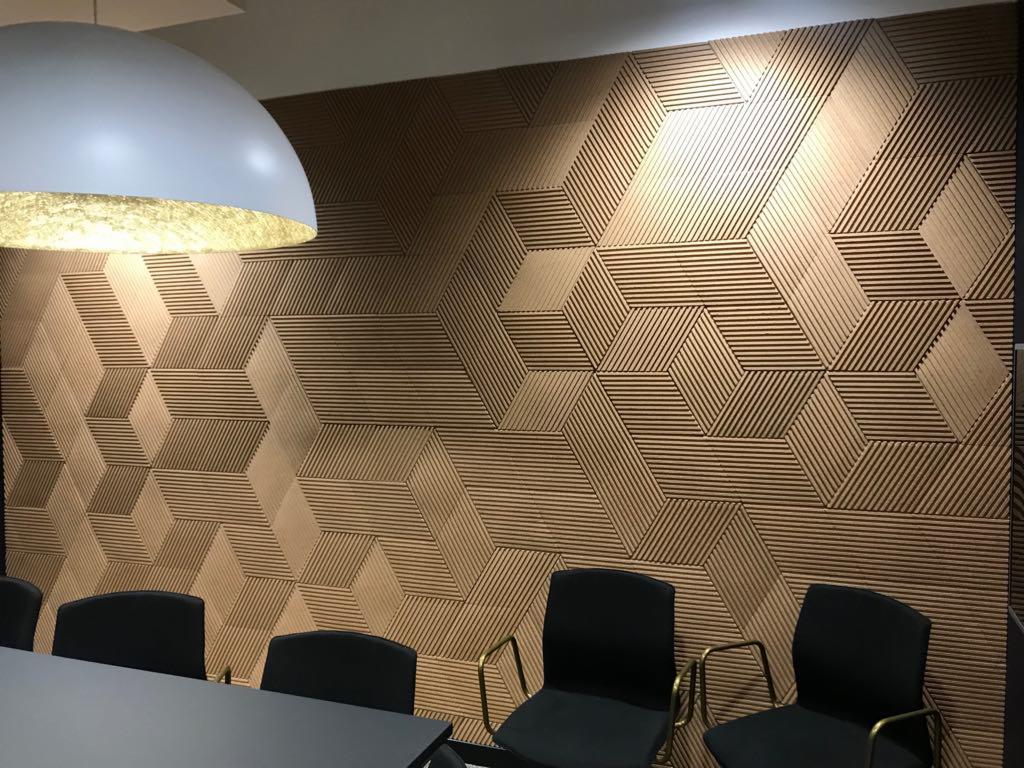 Dekoracyjna ściana z drewnianych paneli 3D w geometryczny wzór, oświetlona lampą wiszącą w biurze.